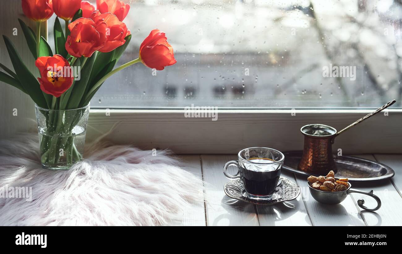 Oriental coffee in traditional Turkish copper coffee pot with flowers on window sill. Rustic wooden window sill with bunch of tulips and book. Cold Stock Photo