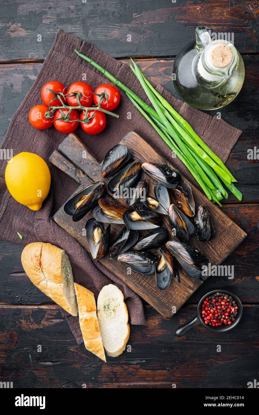Mussels stew in white wine and herbs, on wooden cutting board, on old dark wooden table background, top view flat lay Stock Photo