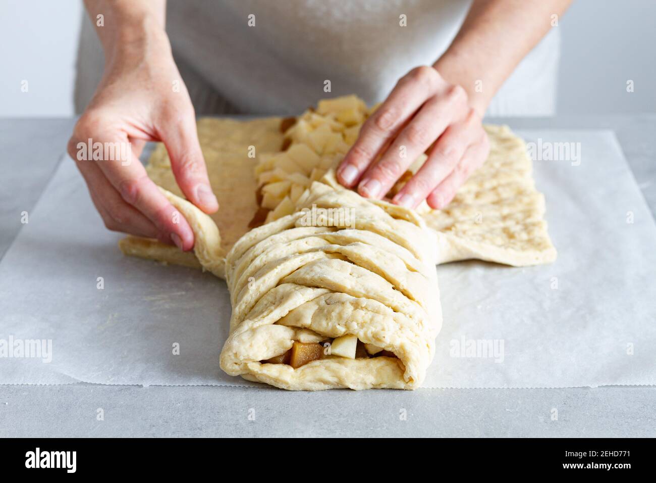 Crop unrecognizable female chef preparing delicious apple pastry with soft braided dough and fruit slices in house Stock Photo