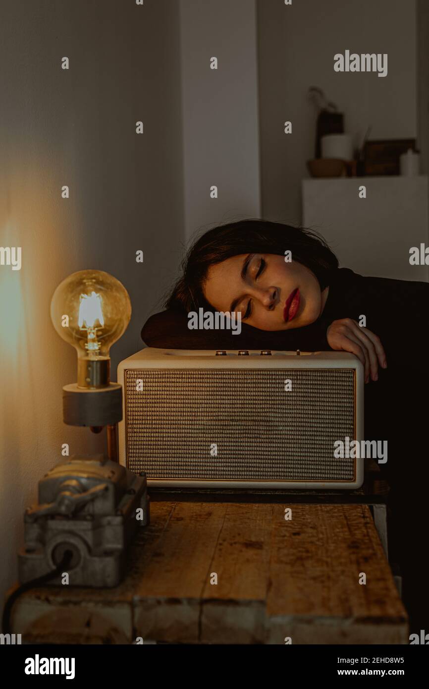 Side view of dreamy female leaning on radio set in retro room and closed eyes Stock Photo