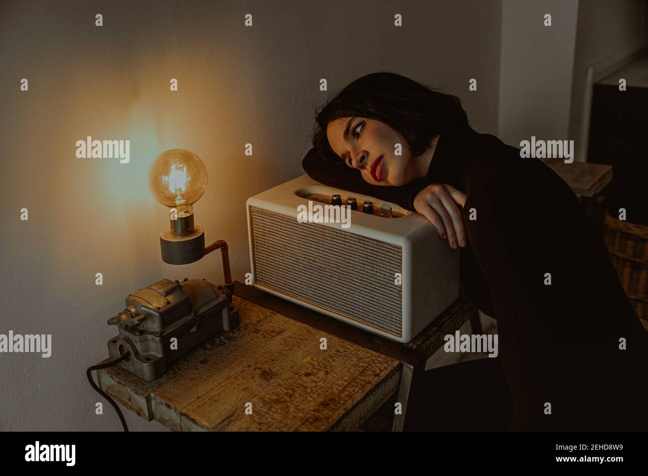 High angle of dreamy female leaning on radio set in retro room and looking at illuminated light bulb Stock Photo