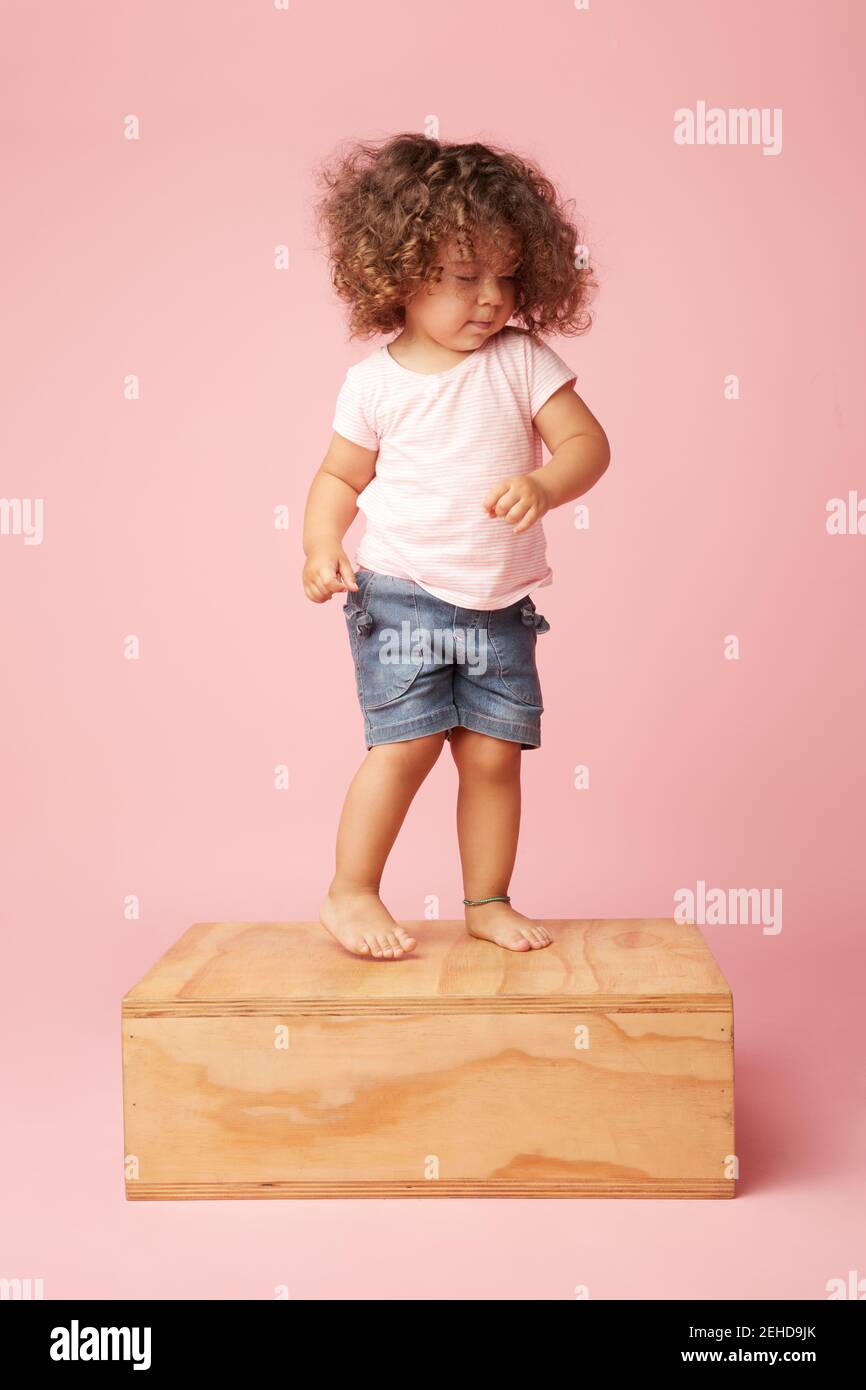 Charming barefoot child in t shirt and denim shorts with curly hair with eyes closed dancing on wooden platform Stock Photo