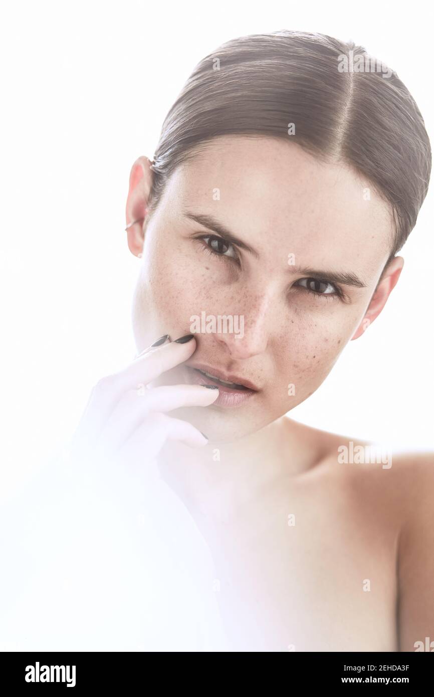 Serious female with makeup and freckles on nose gently touching skin and looking away Stock Photo