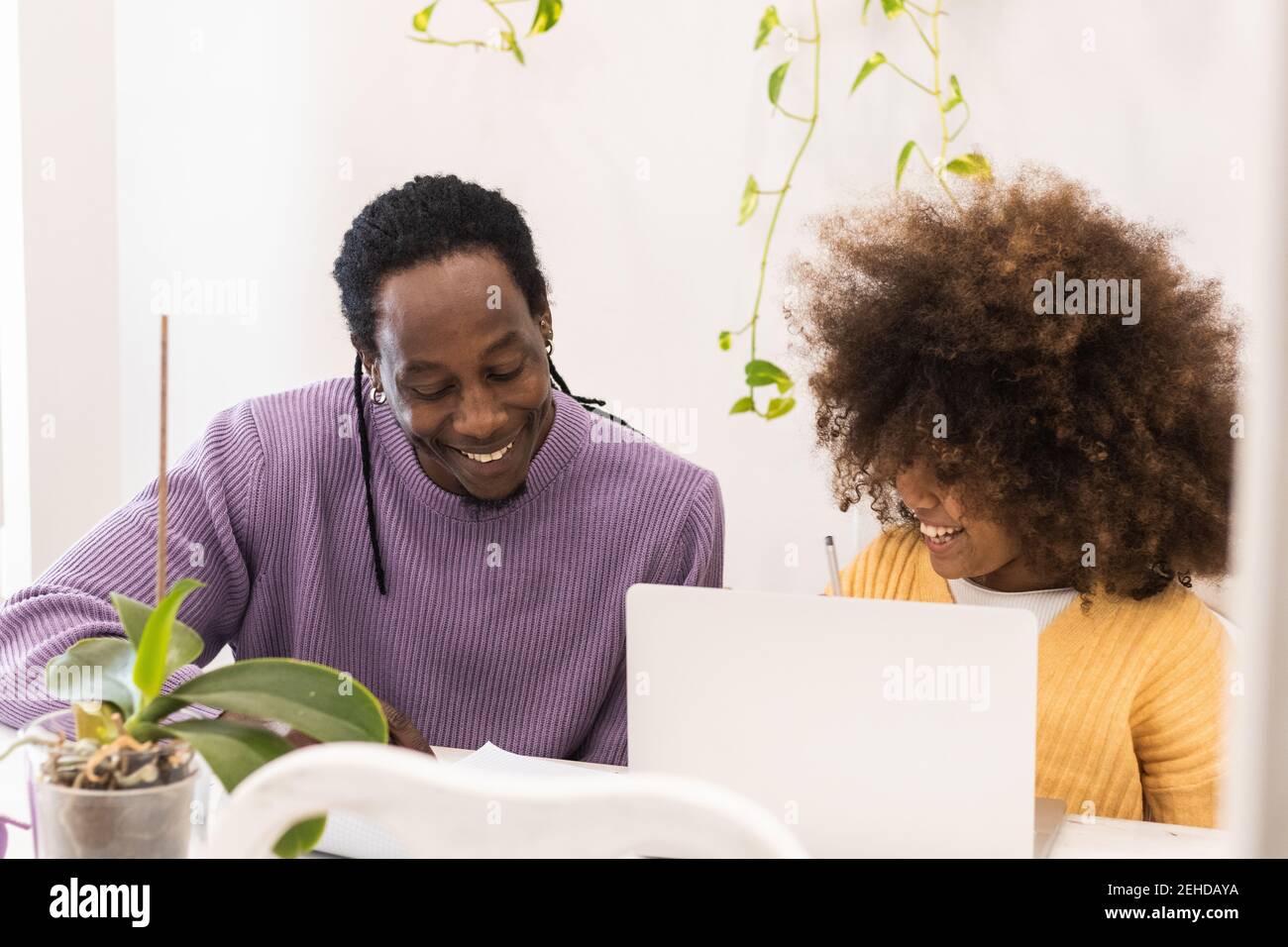 Positive African American dad sitting next to daughter using netbook while doing studies at home Stock Photo