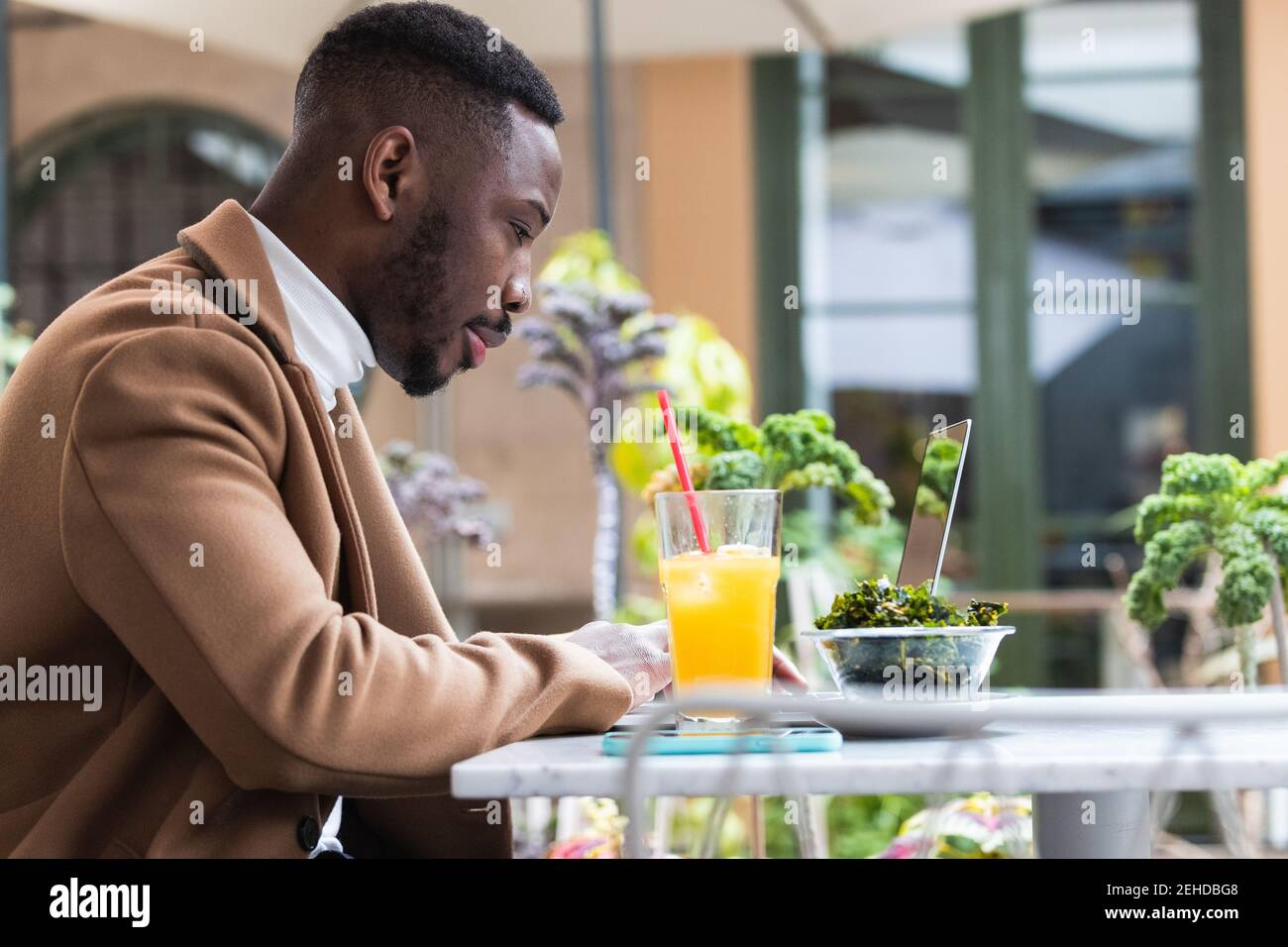 Young African American businessman browsing on laptop while looking down at cafeteria table Stock Photo