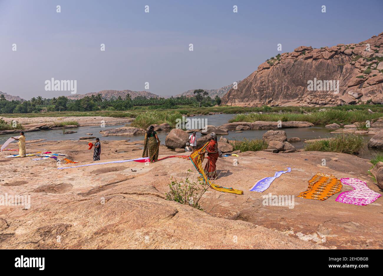 Anegundi, Karnataka, India - November 9, 2013: Navabrindavana island. Colorful saris dry on brown rocks after bath in Tungabhadra River in front of ta Stock Photo