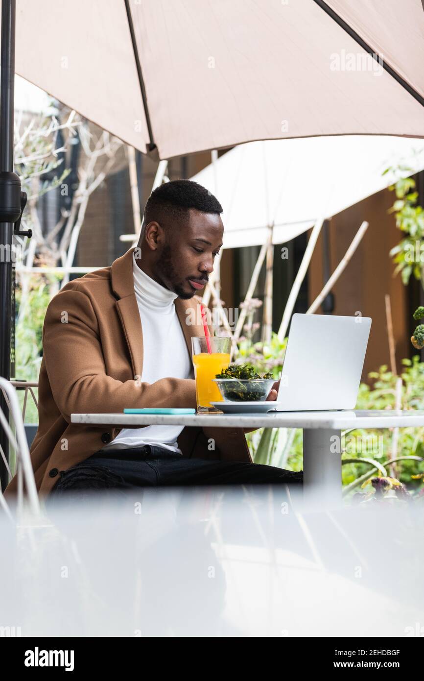 Young African American businessman browsing on laptop while looking down at cafeteria table Stock Photo