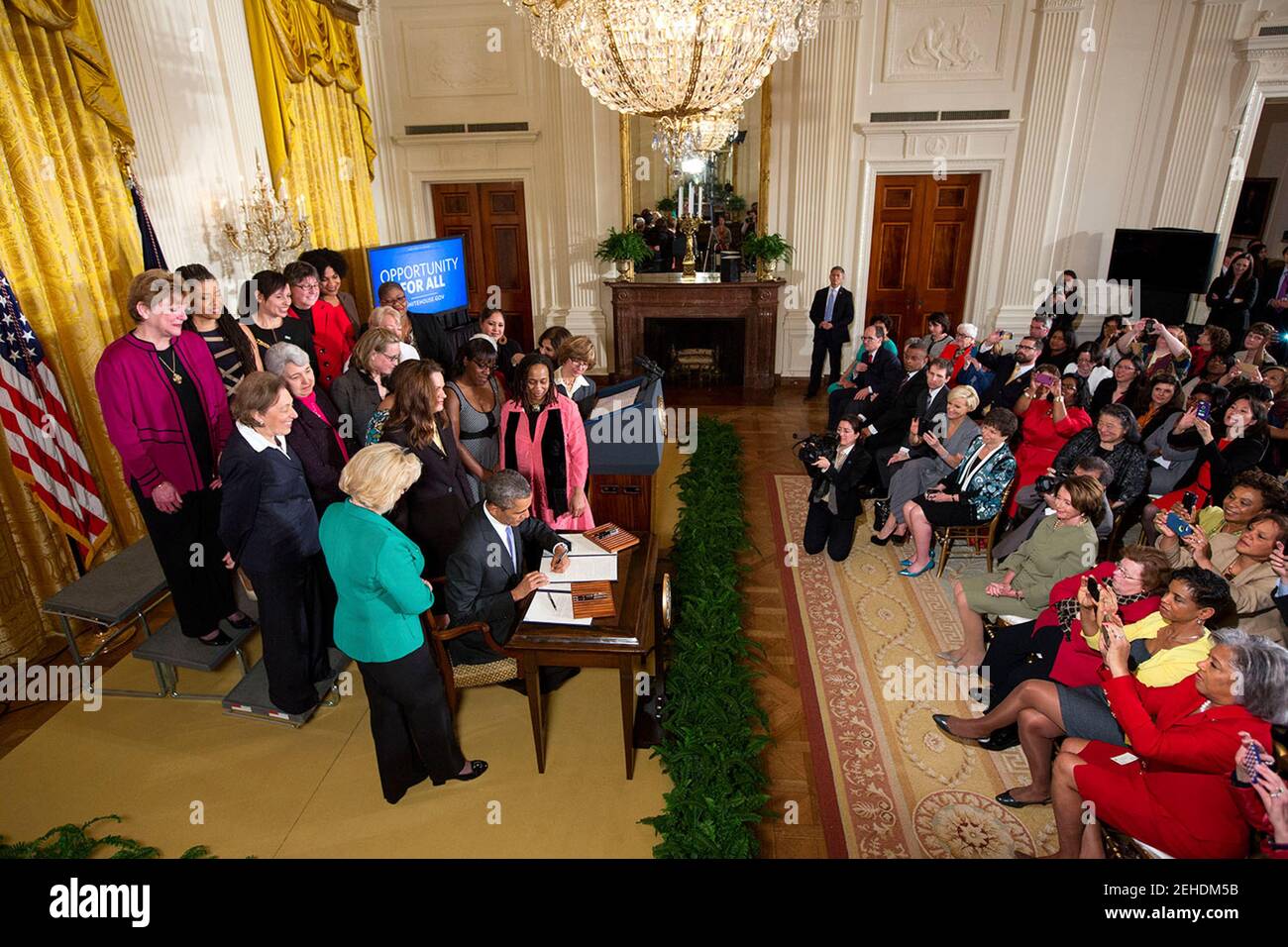 President Barack Obama signs executive actions to strengthen enforcement of equal pay laws for women, at an event marking Equal Pay Day in the East Room of the White House, April 8, 2014. The President signs the Presidential Memorandum -- Advancing Pay Equality Through Compensation Data Collection, and an Executive Order regarding Non-Retaliation for Disclosure of Compensation Information. Lilly Ledbetter stands to the left of the signing table. Stock Photo