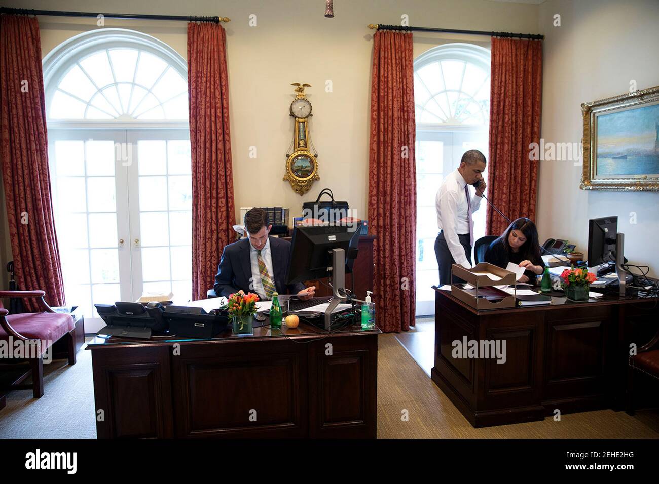 President Barack Obama talks on the phone in the Outer Oval Office, June 12, 2014. Brian Mosteller, Director of Oval Office Operations and Ferial Govashiri, Personal Assistant to the President, are seated at their desks. Stock Photo