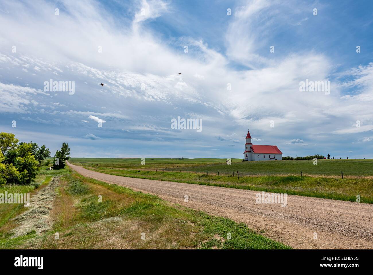 Birds flying over a gravel road in the country leading to the historic St. Martin’s Roman Catholic Church in Billimun, Saskatchewan, Canada Stock Photo