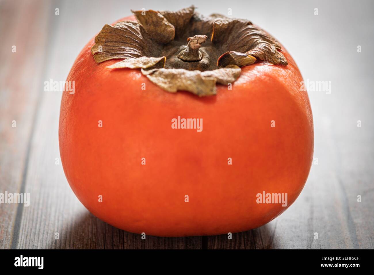 A macro shot with selective focus of a ripe persimmon fruit set on a wood table. Stock Photo