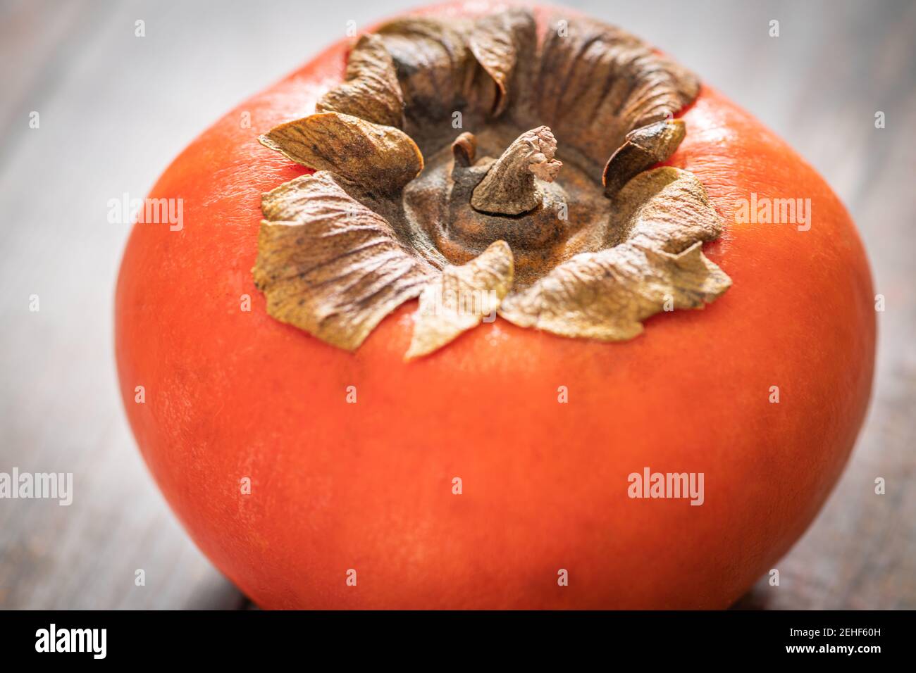 A macro shot with selective focus of a ripe persimmon fruit set on a wood table. Stock Photo