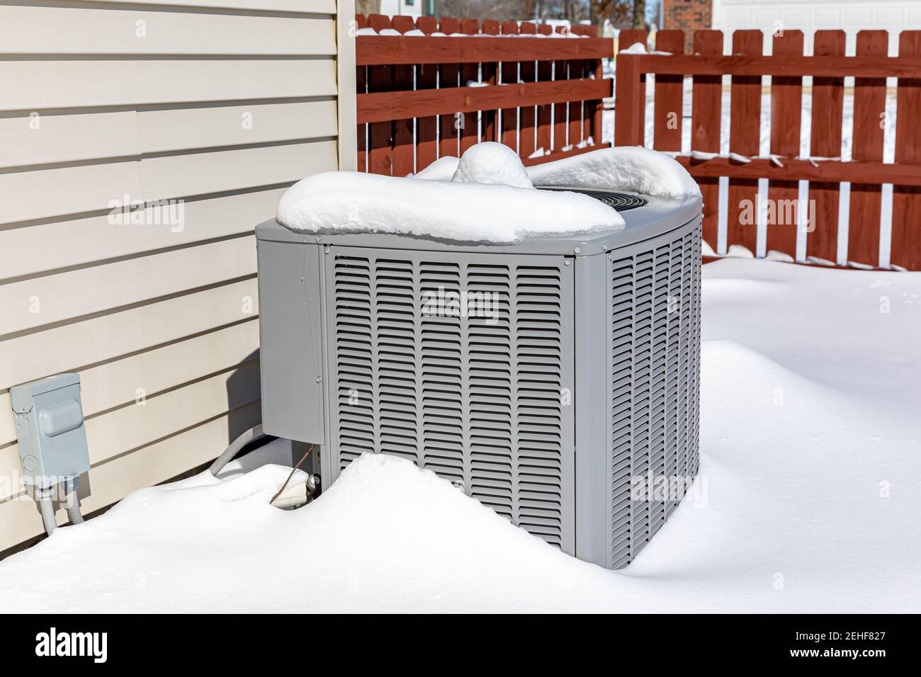 House air conditioning unit covered in snow during winter. Concept of home air conditioning, hvac, repair, service, winterize and maintenance. Stock Photo