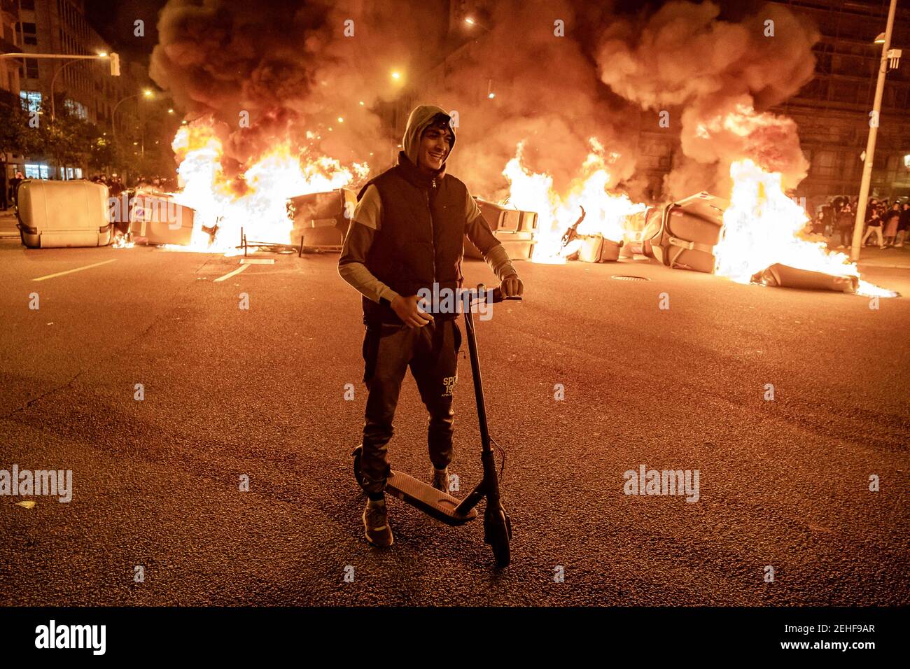 A protester on an electric scooter standing close to a large burning  barricade on Avenida Marqués de la Argentera during the fourth night of  protests and riots in response to the arrest
