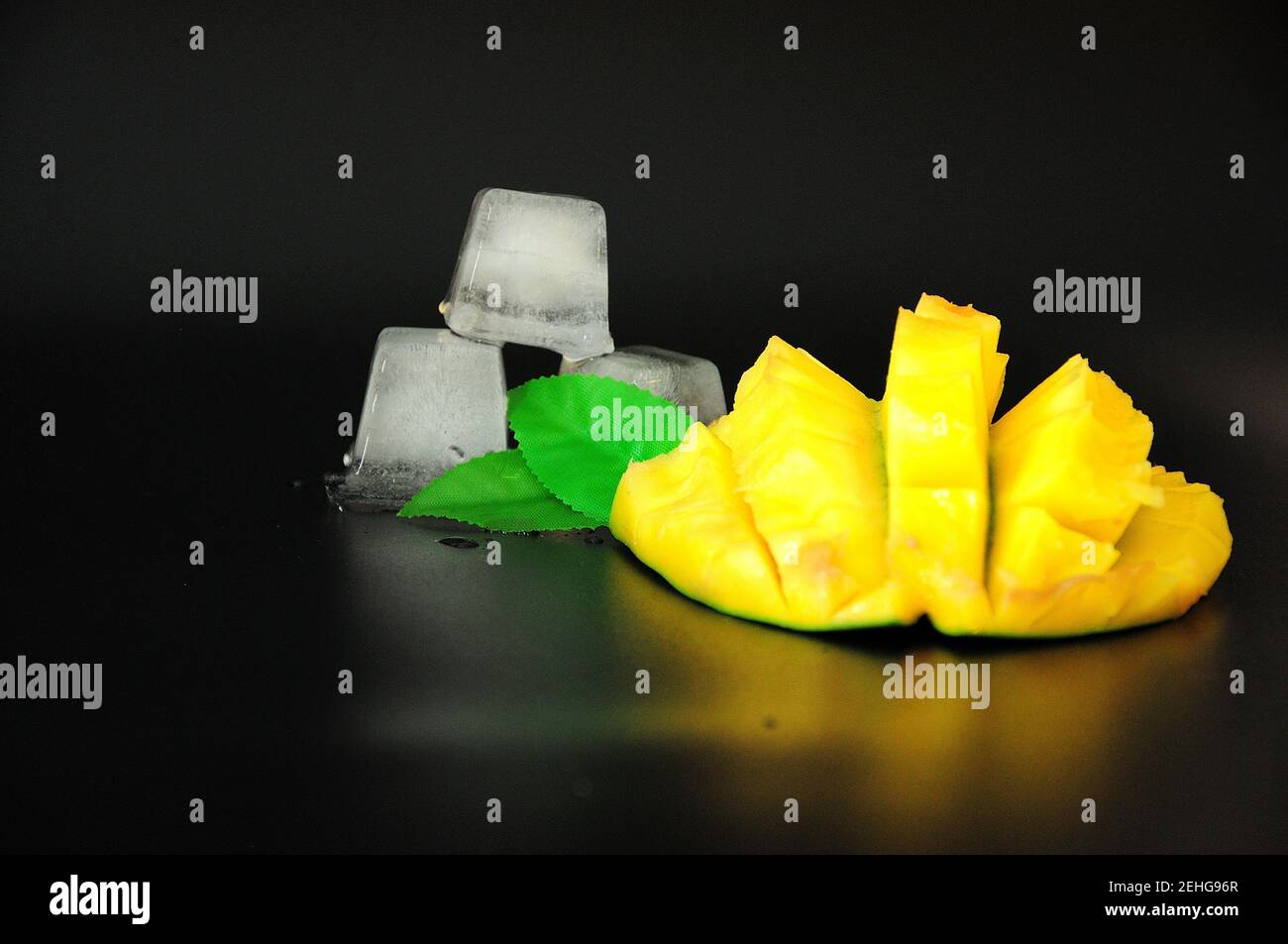 Diced mango pulp and melted ice cubes on a black background. Closeup