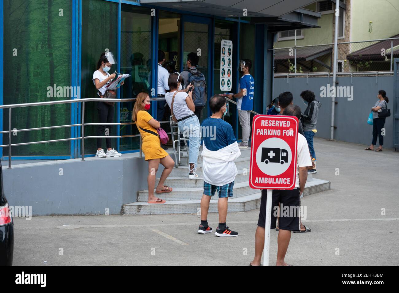 Men and women wait outside of a clinic wearing face masks and shields also being socially distant, Cebu City, Philippines Stock Photo