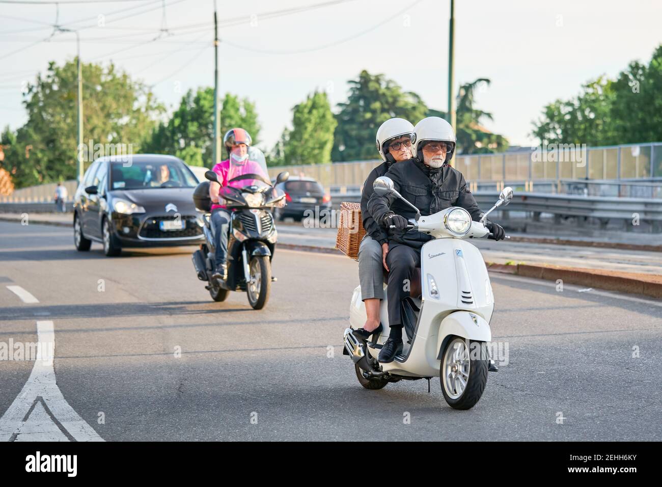 Senior couple riding motorbike in busy city street traffic. Motorcyclists driving motorcycle and cars on the road. Milan, Italy - May 26, 2020 Stock Photo