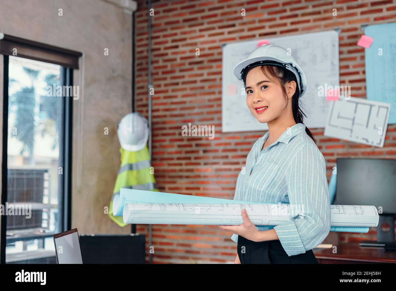 Portrait Asian engineer woman hold engineer drawing design blue print at room site construction. Stock Photo