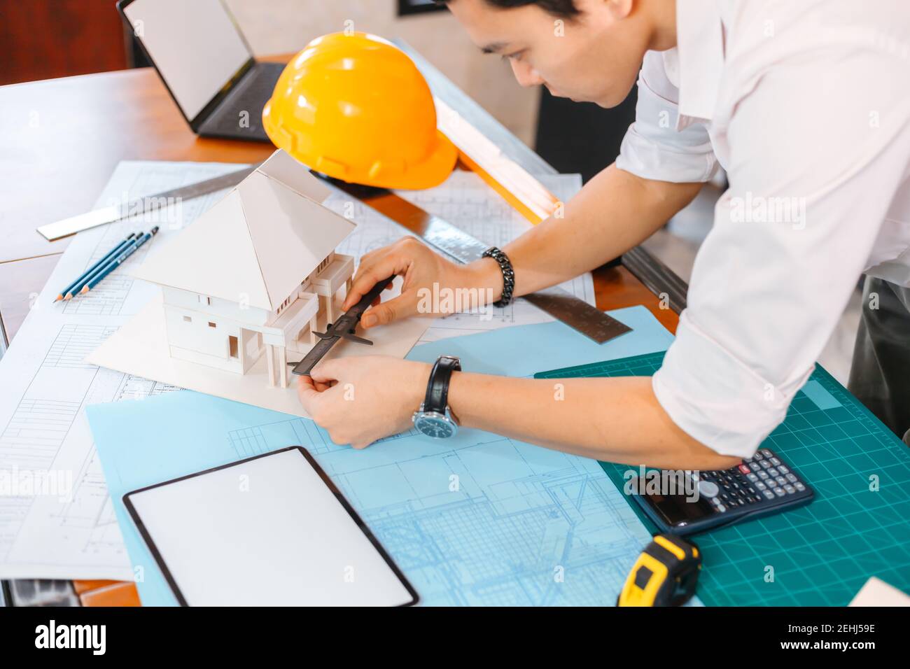 Engineering hands hold vernier caliper working and checking house model scale between meeting with businessman and businesswoman. Stock Photo