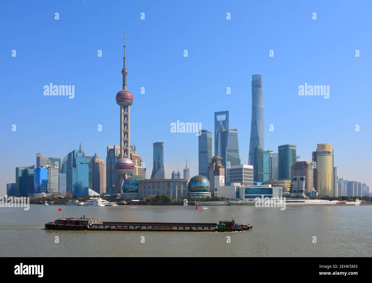 Barge transports goods along the Huangpu river, part of the Beijing to Hangzhou grand canal. Pudong skyline in the background. Feb 2021 Stock Photo