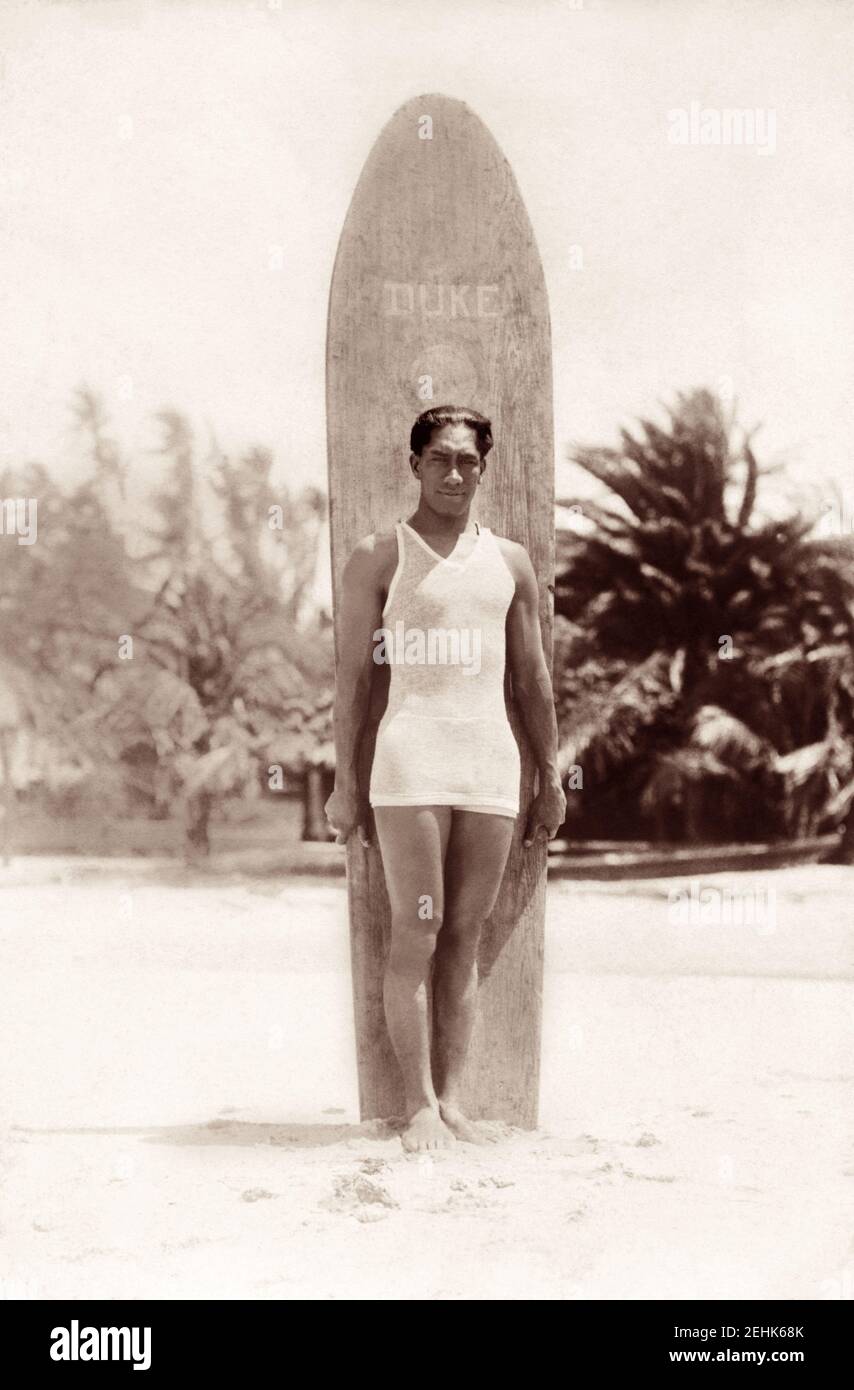 Duke Paoa Kahanamoku (1890–1968), the father of modern surfing, standing on a beach in Hawaii with his wooden surfboard, c1915. Stock Photo