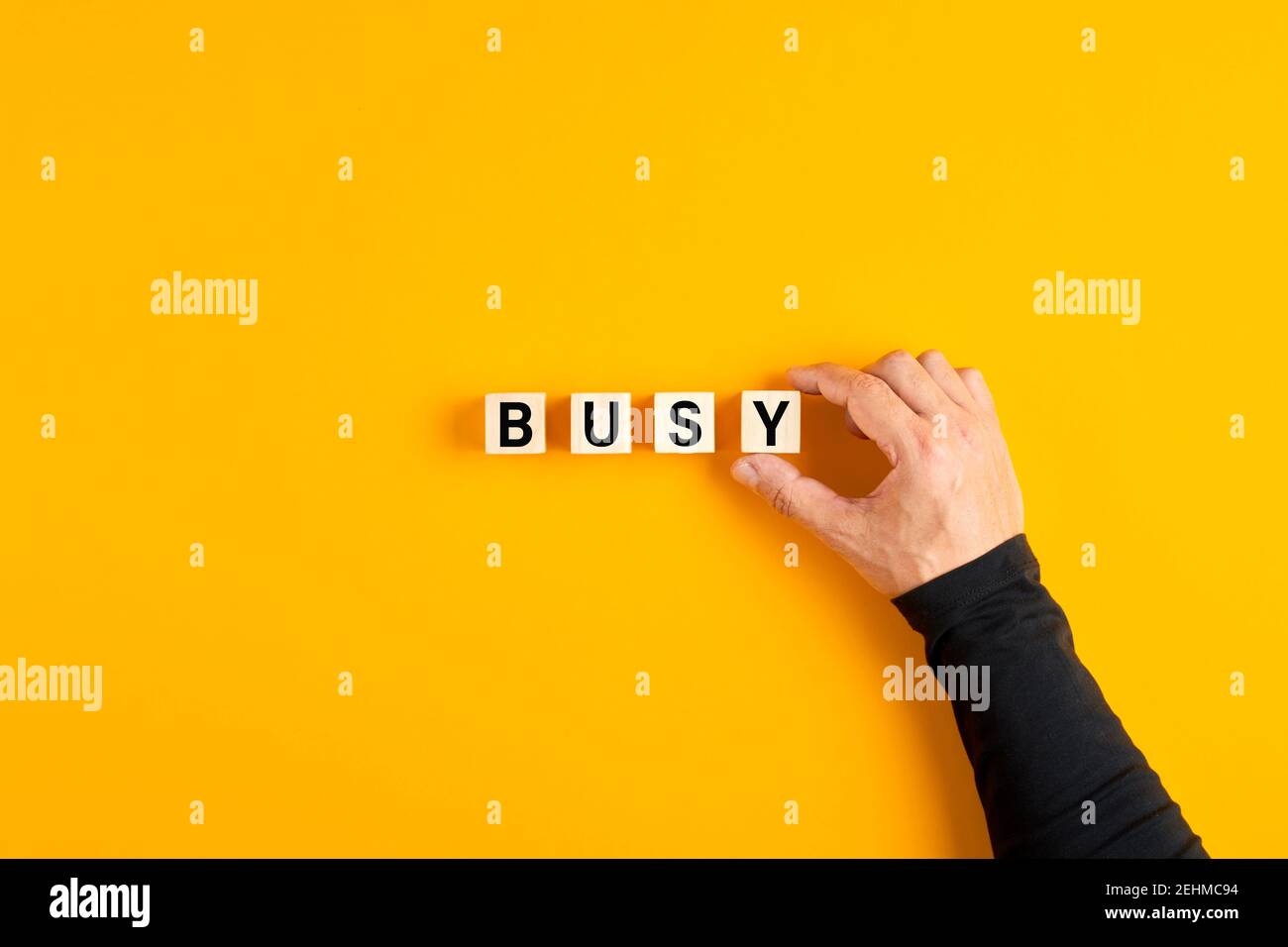 Male hand placing the wooden cubes with the word busy on yellow background. Overwork, stress or occupied concept. Stock Photo