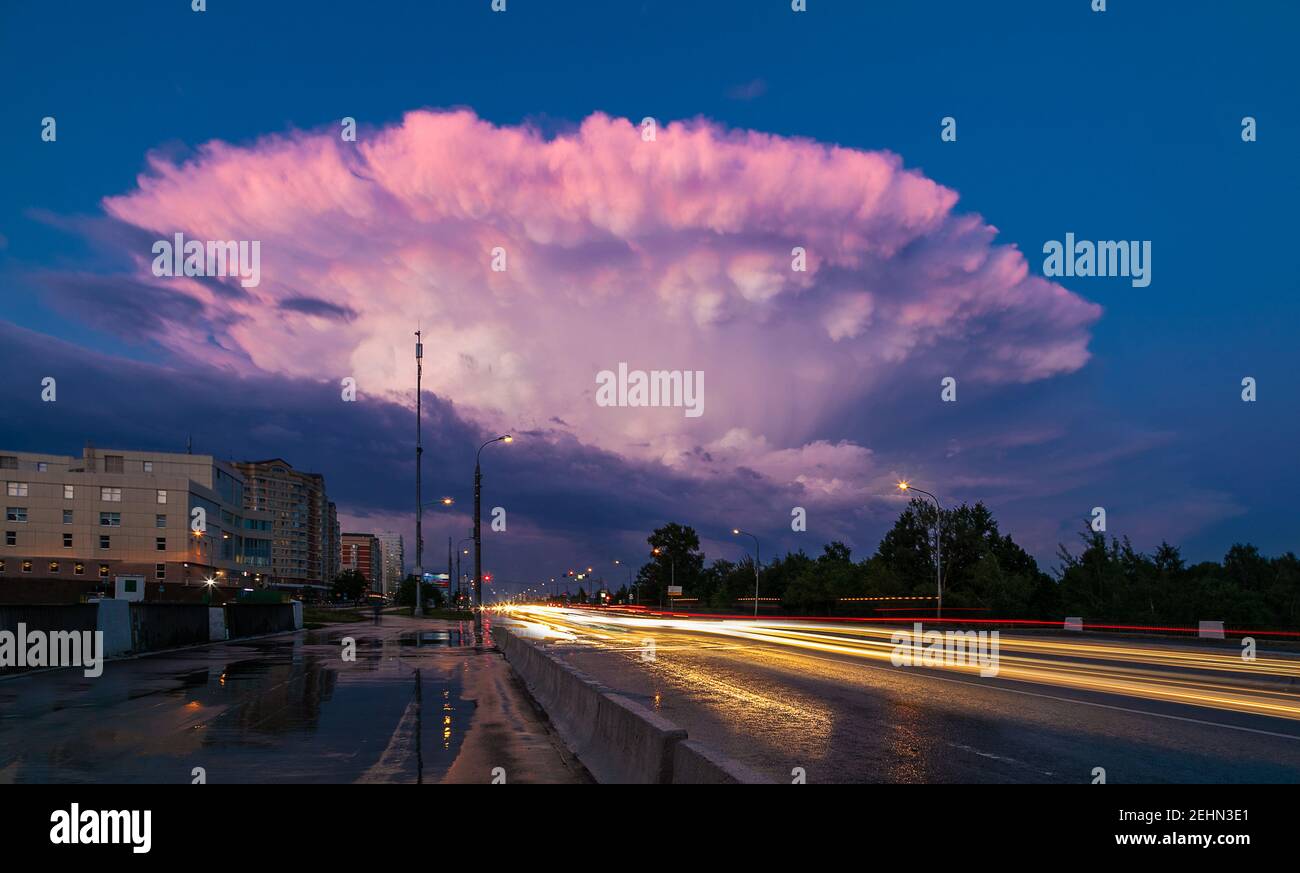 A large pink cloud in the form of a mushroom, in the evening after the rain. Glowing lights from the cars. Tracer beam. Tinting Stock Photo