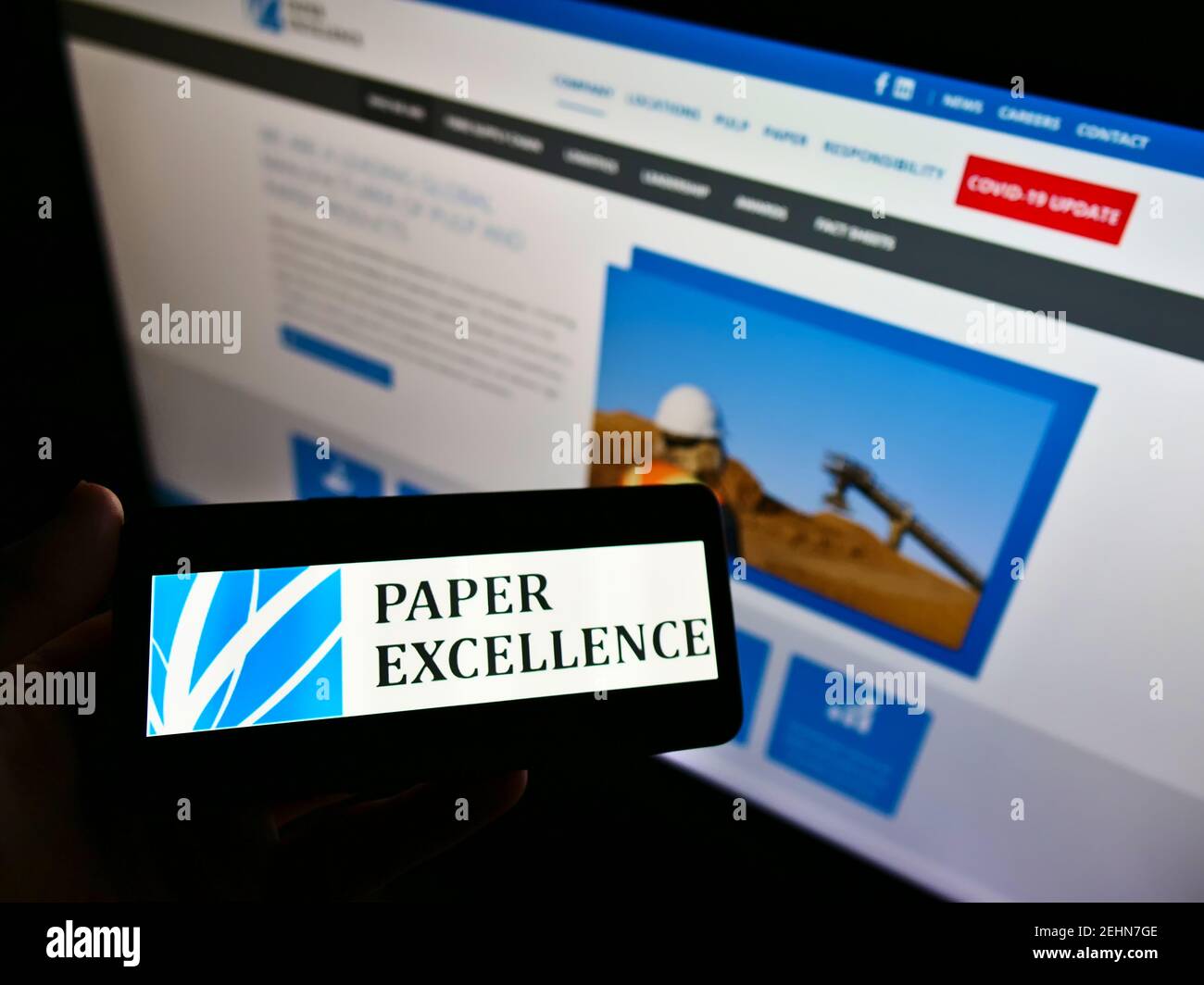 Person holding mobile phone with logo of Canadian pulp manufacturer Paper Excellence B.V. on screen in front of web page. Focus on cellphone display. Stock Photo