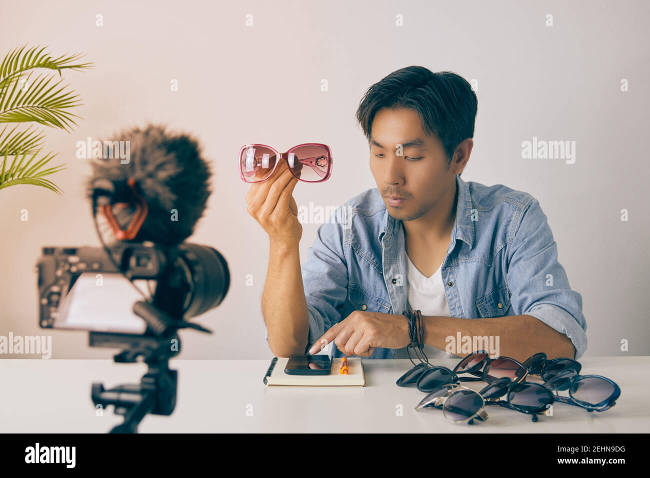 Asian Vlogger or Blogger Show Pink Fashion Glasses and Using Smartphone to Chat with Customer and Recording Video. Freelancer Online Live Streaming wi Stock Photo