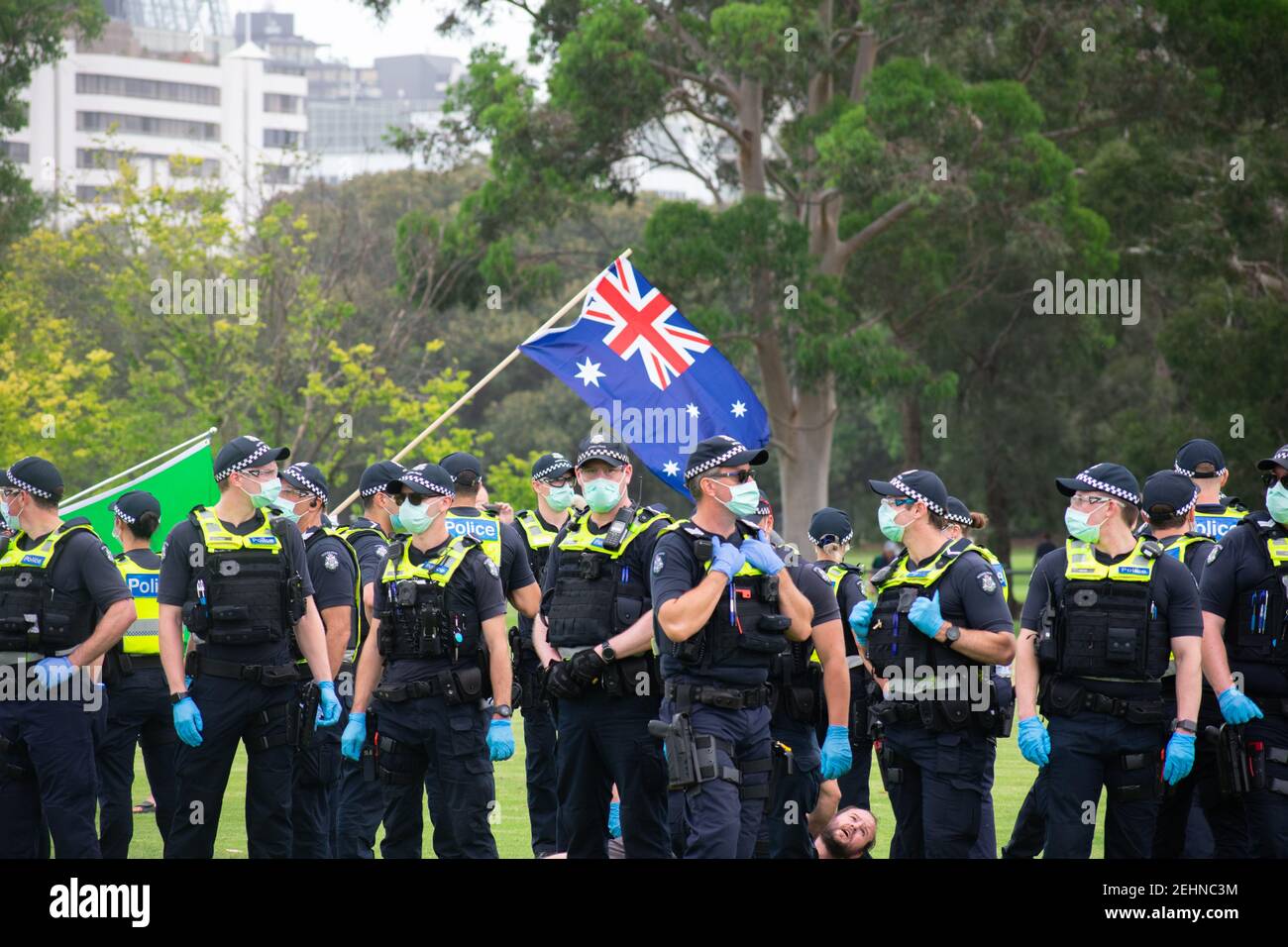 Melbourne, Australia. 20th Feb 2021. Police stand guard around a protester on the ground while the Australian flag flies over head at an anti COVID vaccination march in Fawkner Park. February 20, 2021. Melbourne, Australia. Credit: Jay Kogler/Alamy Live News Stock Photo