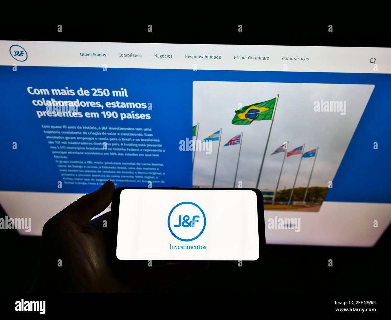 Person holding smartphone with logo of Brazilian investment company J and F Investimentos S.A. on screen in front of website. Focus on phone display. Stock Photo