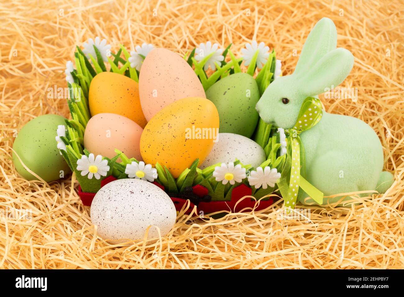 Easter colorful eggs in basket and green bunny on straw background ...