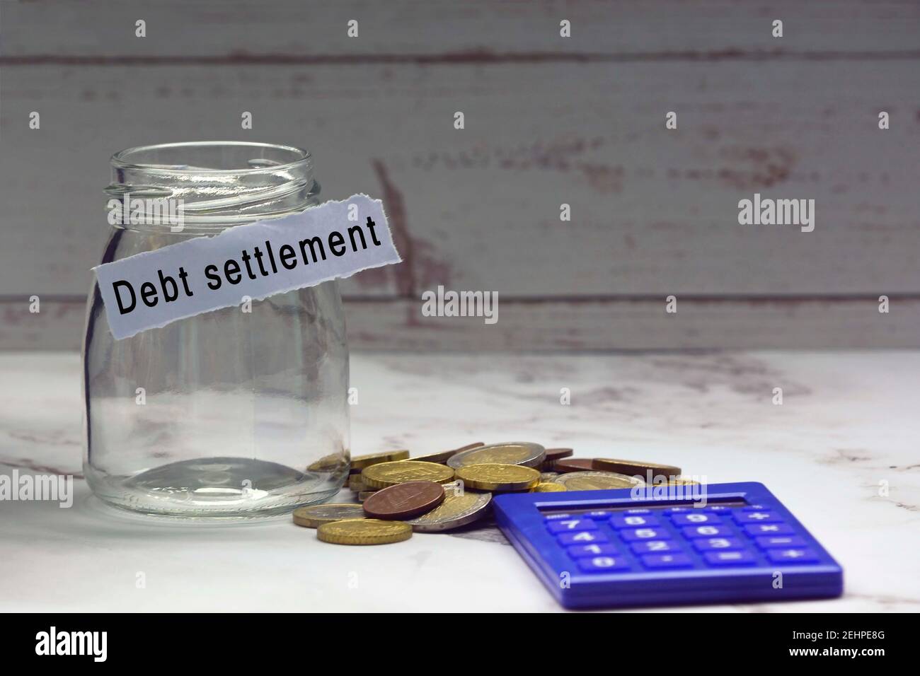 Glass jars with blurred multicurrency coins, calculator and text on white torn paper - Debt settlement Stock Photo