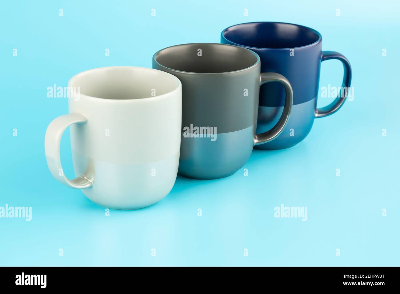 Three ceramic cups isolated on blue background. Stock Photo