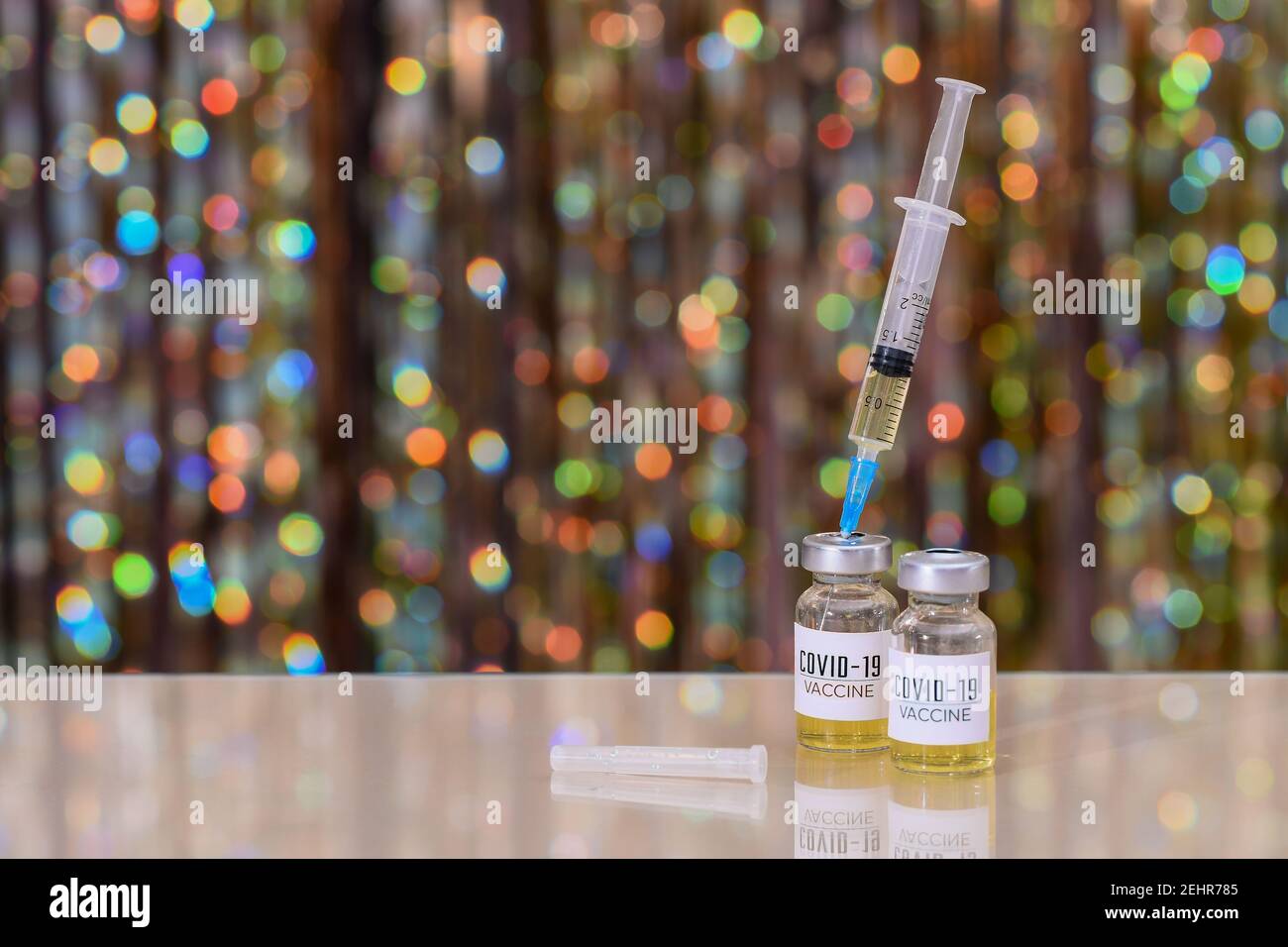 A bottle of of coronavirus vaccine. The syringe is inserted into a bottle with the covid-19 vaccine. On a shiny bokeh background.  Stock Photo