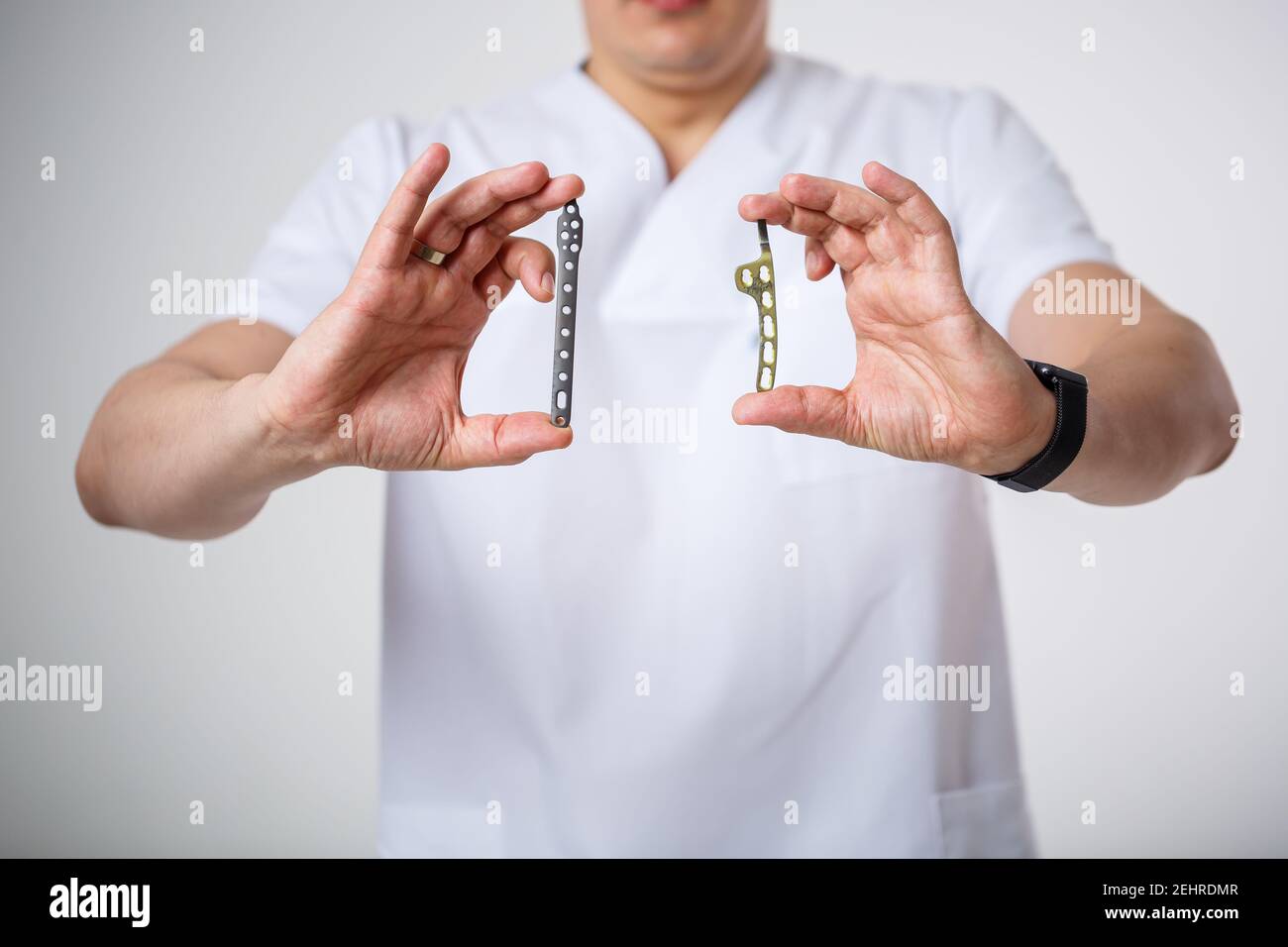 Young male doctor in white surgical suit holds and examines titanium