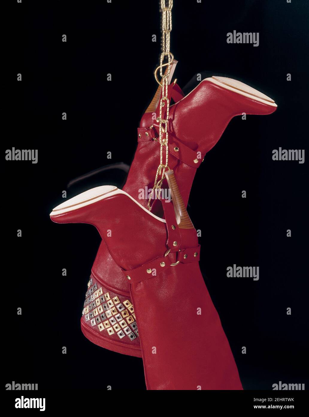 Composition of two women's red boots hanging on a gold chain. Isolated on black. Stock Photo