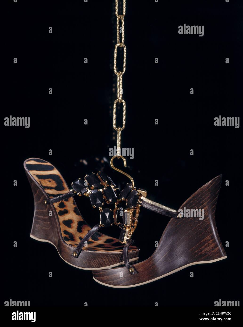 Elegant composition of two women's sandals with black stones and leopard sole, hanging on a gold chain. Stock Photo