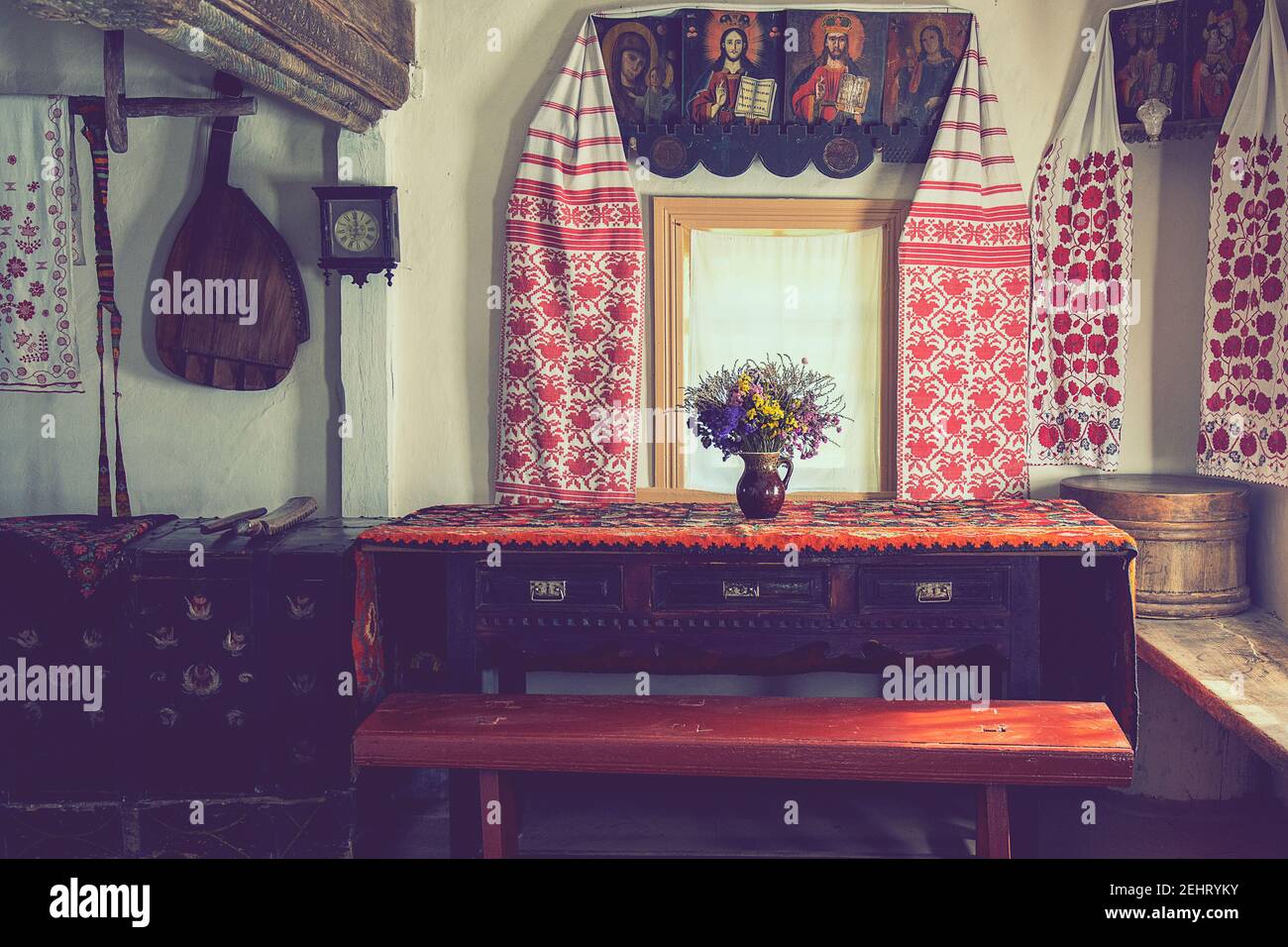 Ethnic towels, bunch of dry flowers and historical icons on white walls. Wood benches near the window.Vintage interior room in the national Museum of Stock Photo