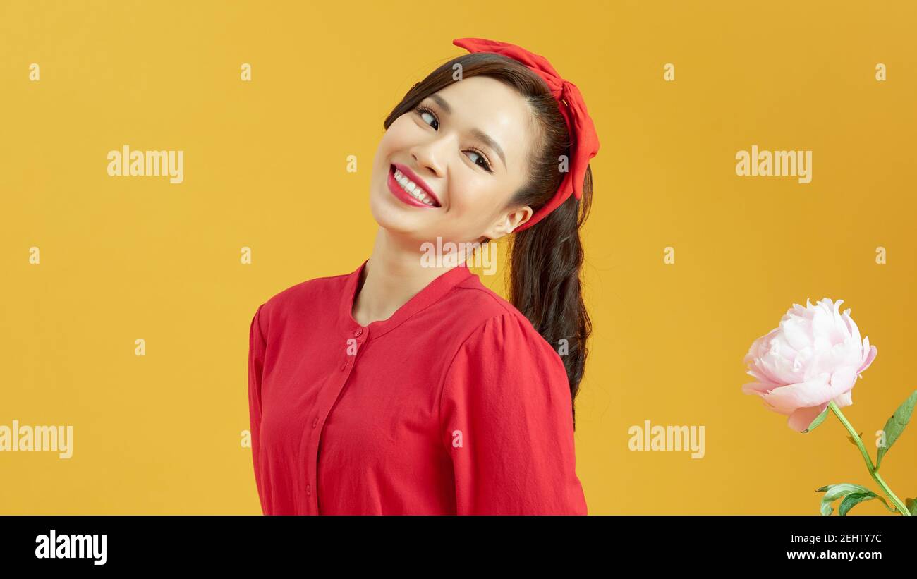 Portrait of a pretty lovely young girl casually dressed standing isolated over yellow background, near peony flower Stock Photo