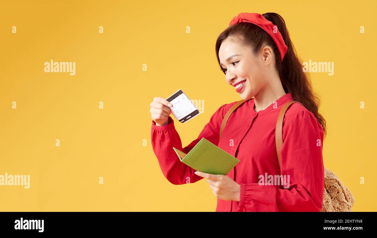 Cheerful girl holding passport, plane ticket and passport before yellow background, Stock Photo