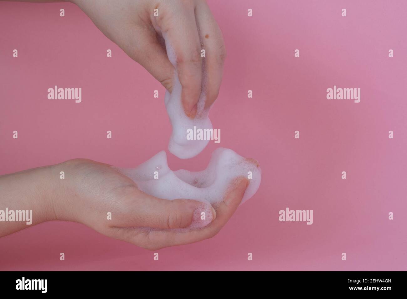 Close up of woman's hands with face foam, hand foam on pink background