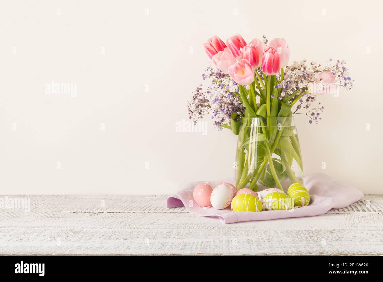 Spring Easter composition with bouquet of pink tulips and painted eggs on light background. Space for text. Stock Photo