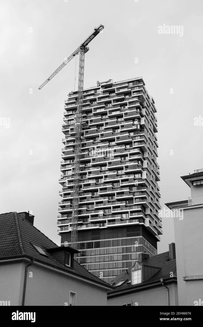 Vertical grayscale shot of a tower crane and a new residential building against a cloudy sky Stock Photo