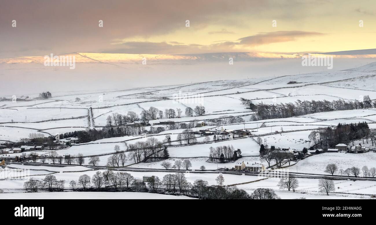 A view of the snow covered North Pennines with the sun kissing the tops of the fells. The A689 runs through the scene. Weardale, County Durham. Stock Photo