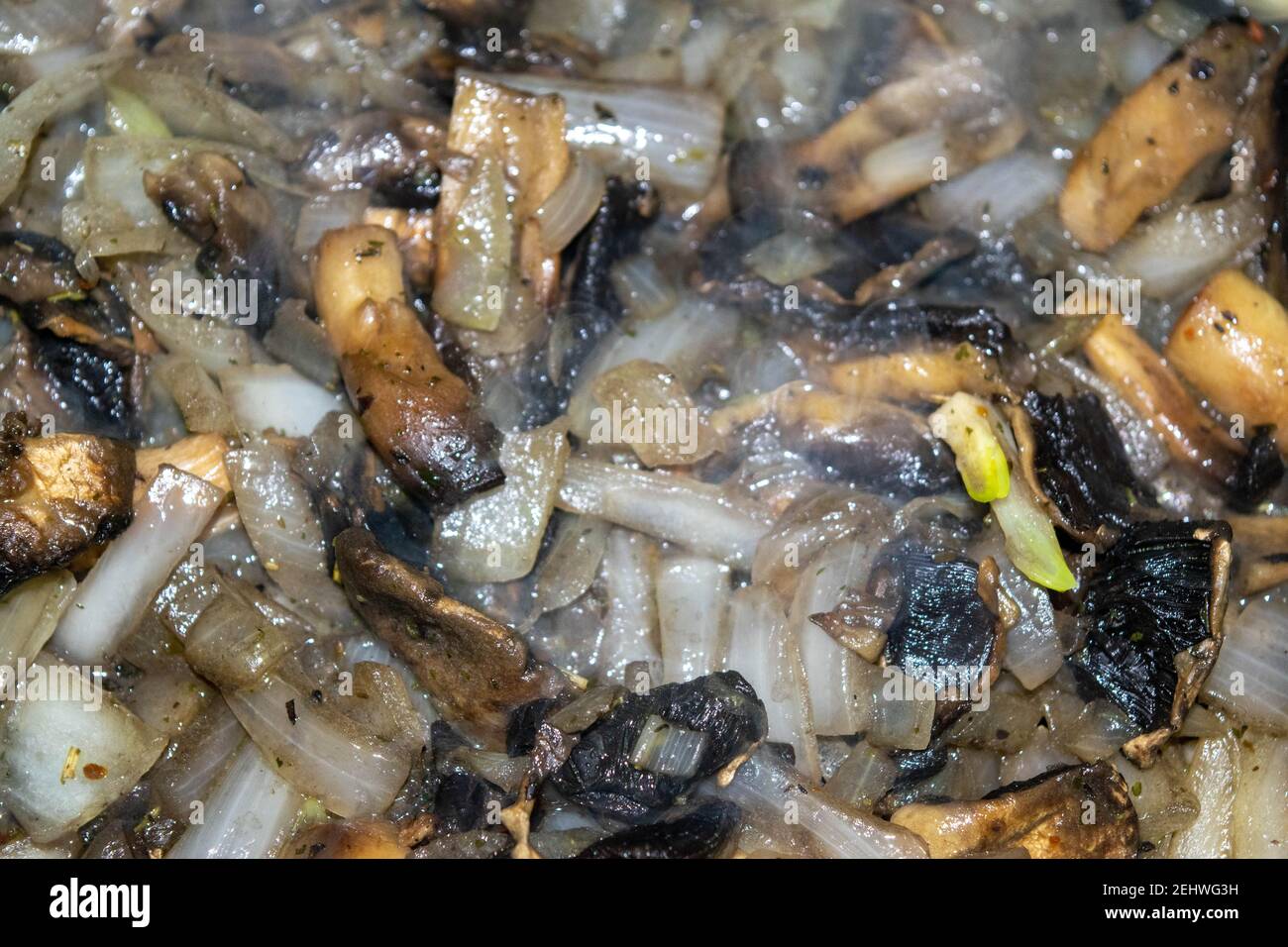 Wild mushrooms with onions are fried in a frying pan. Autumn harvest. Close-up, selective focus, surface texture. Stock Photo