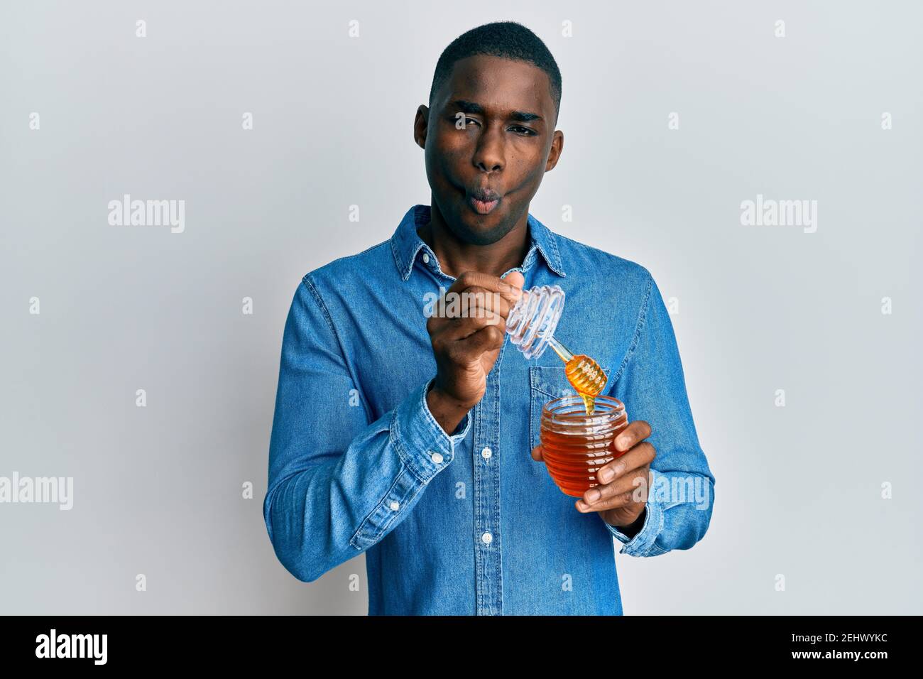 Young african american man holding honey making fish face with mouth and squinting eyes, crazy and comical. Stock Photo