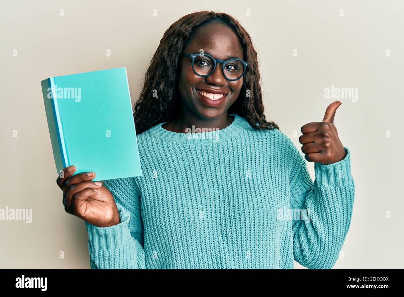 African young woman reading a book wearing glasses smiling happy and positive, thumb up doing