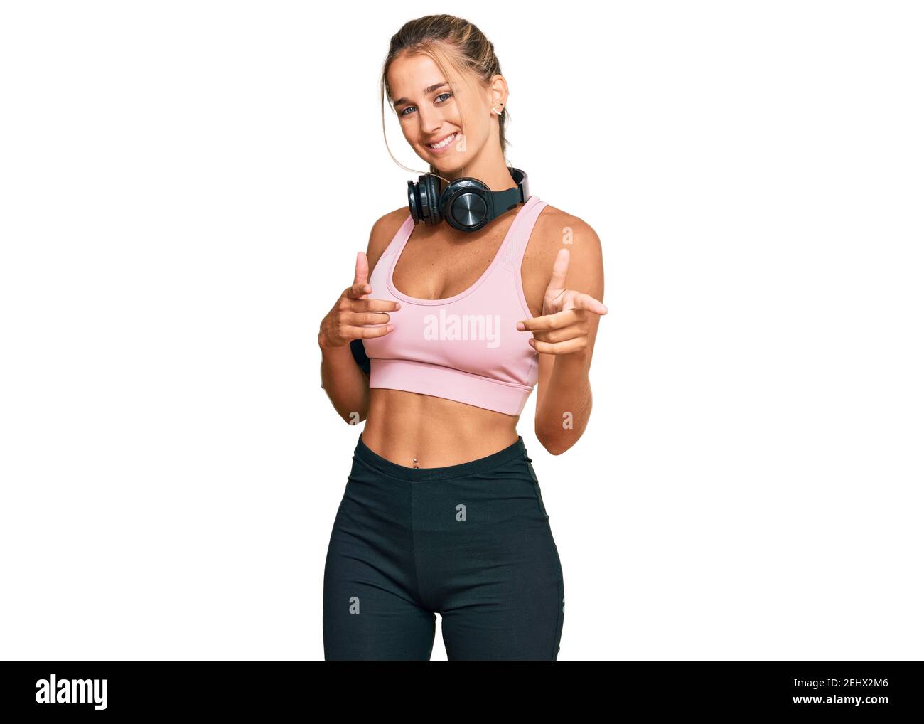 Young blonde woman wearing gym clothes and using headphones pointing  fingers to camera with happy and funny face. good energy and vibes Stock  Photo - Alamy