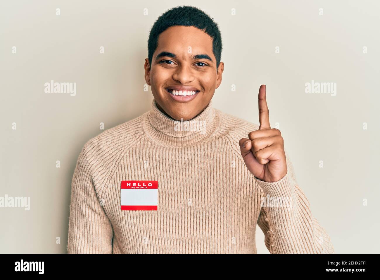 Young handsome hispanic man wearing hello my name is sticker ...